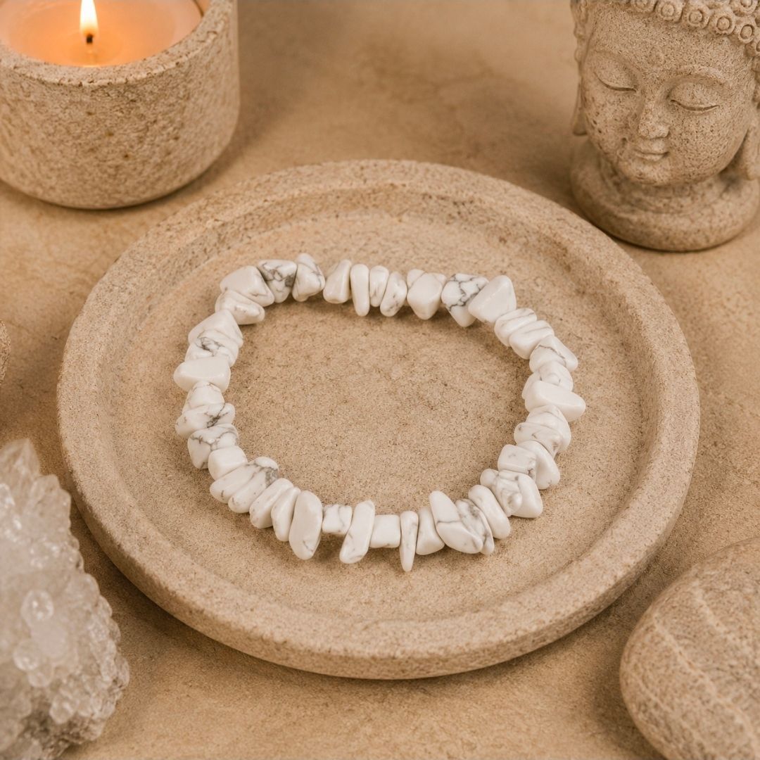Een armband van witte schelpen op een beige stenen schaal, met een brandende kaars en een Boeddhabeeldje ernaast.