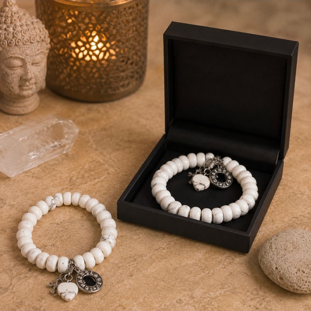 Een witte kralenarmband en een bijpassende armband in een zwarte geschenkdoos op een beige tafelblad met decoratieve kaarsen