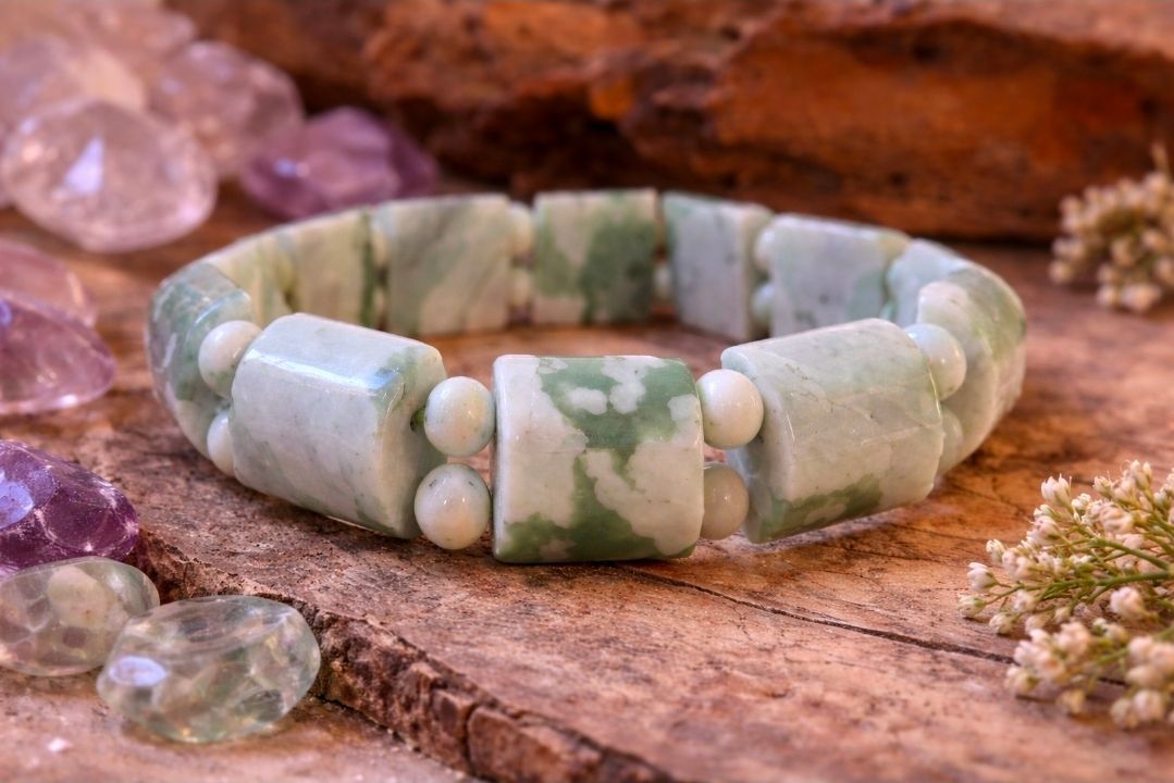 Groen-witte kralenarmband op een rustieke houten ondergrond met roze kristallen in de buurt.