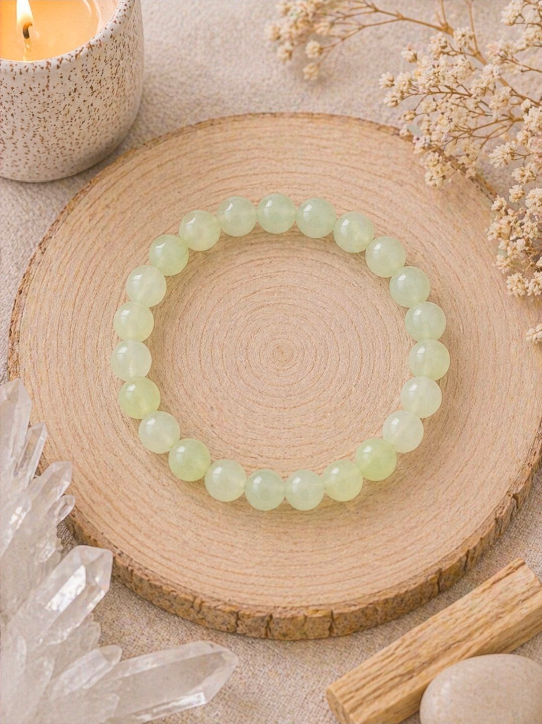 Lichtgroene kralenarmband op een rond houten dienblad met kristallen en gedroogde bloemen.