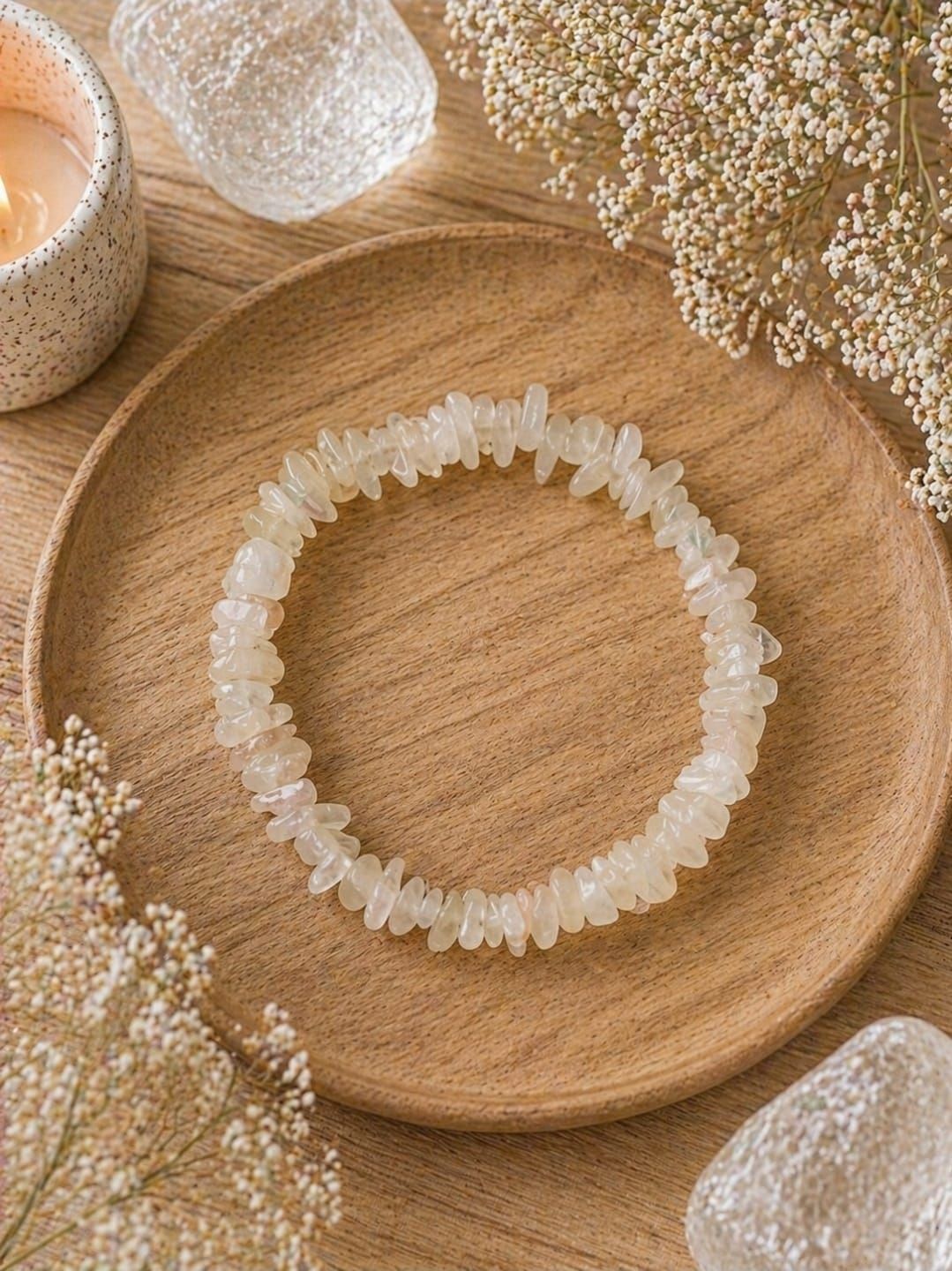 Een wit kralenarmbandje op een houten schaaltje, met zachte, neutrale decoratie en kaarsen in de buurt.