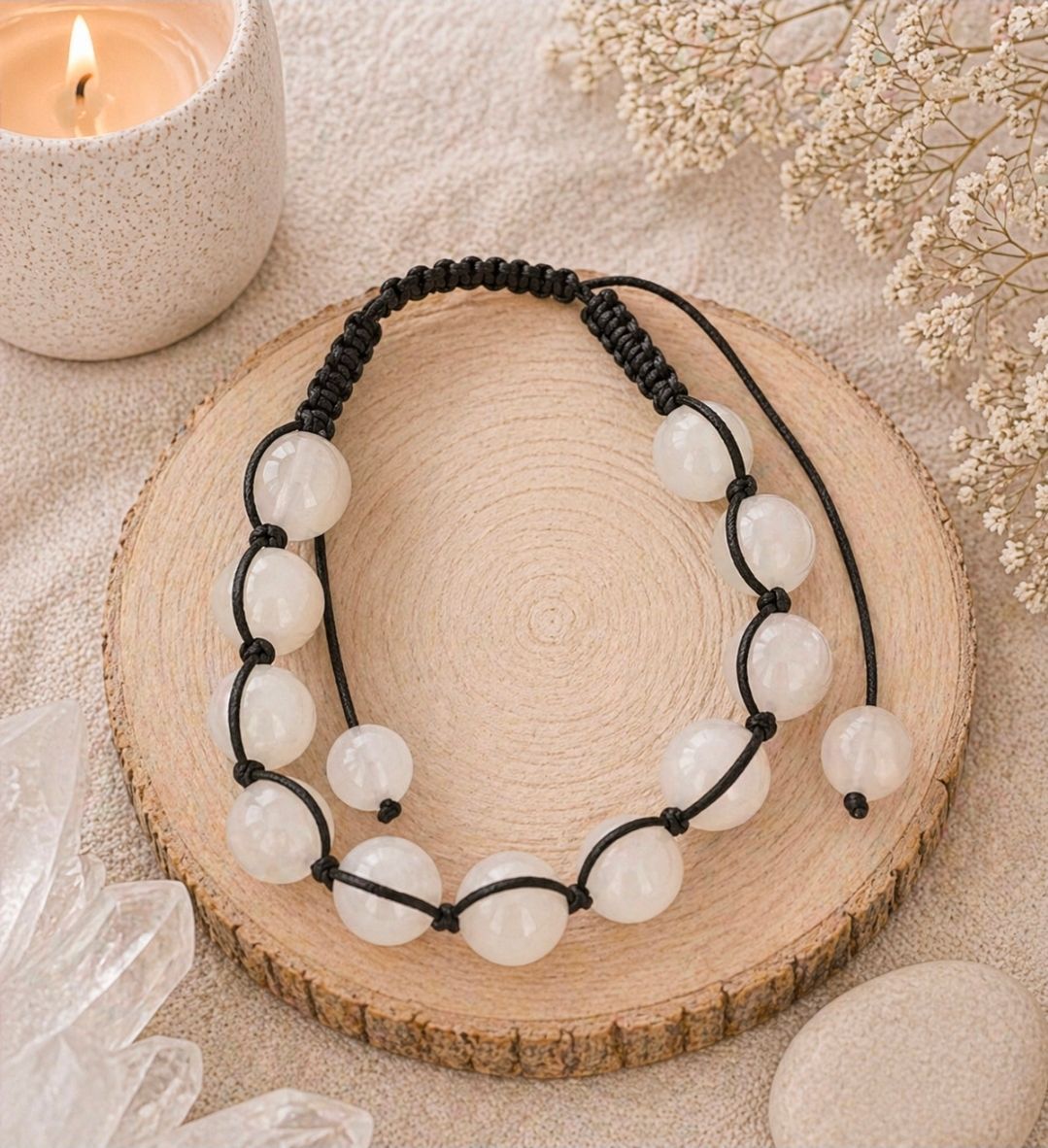Zwarte koordarmband met witte kralen op een houten schijfje, gestyled met een kaars en gedroogde bloemen.