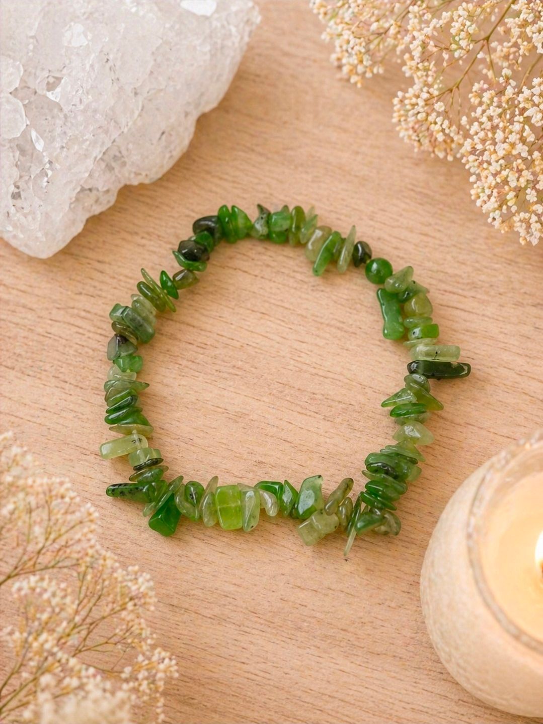 Groene kralenarmband op een houten ondergrond met kristallen en een kaars in de buurt.