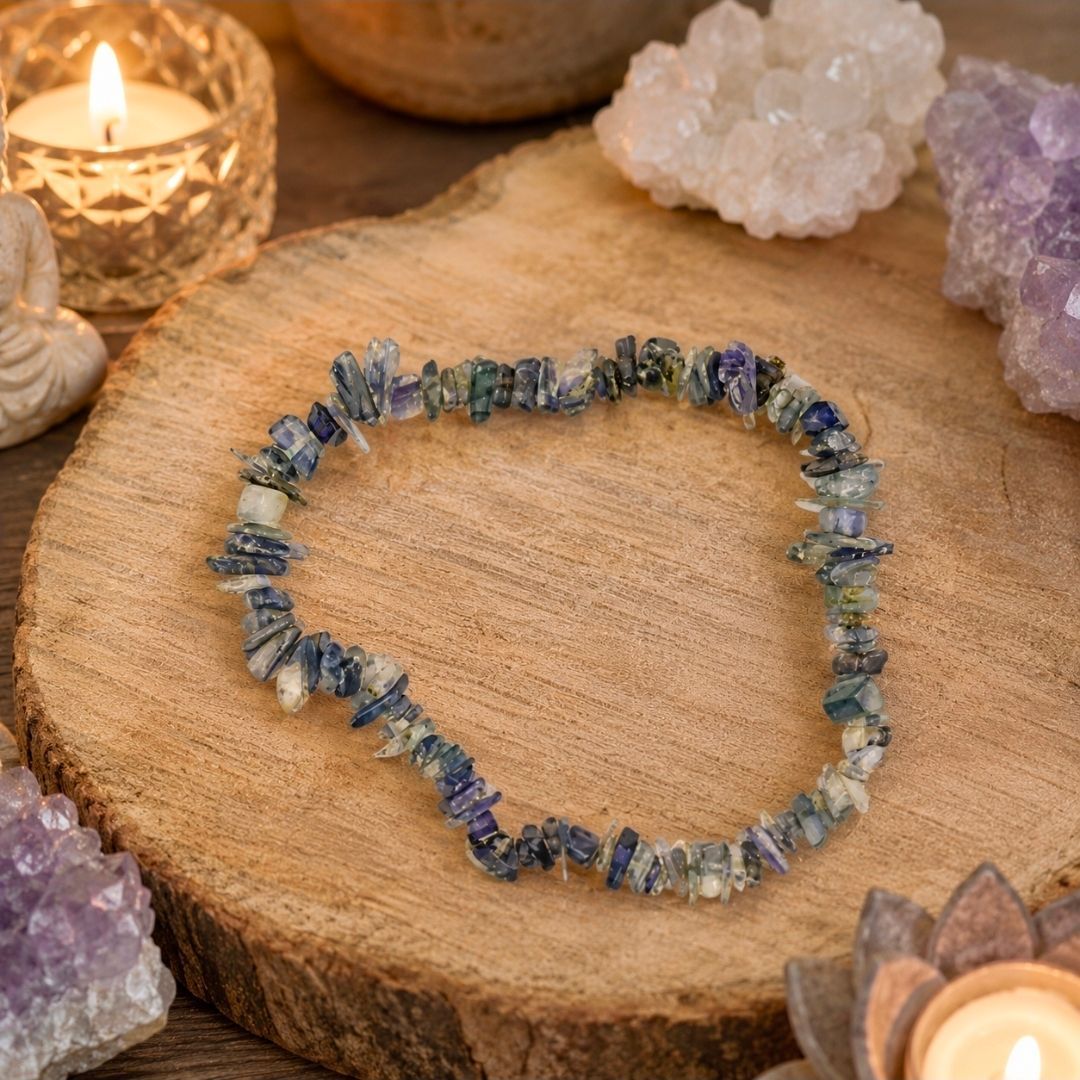 Een blauw-paarse kralenarmband op een houten plank met kristallen en een brandende kaars ernaast.