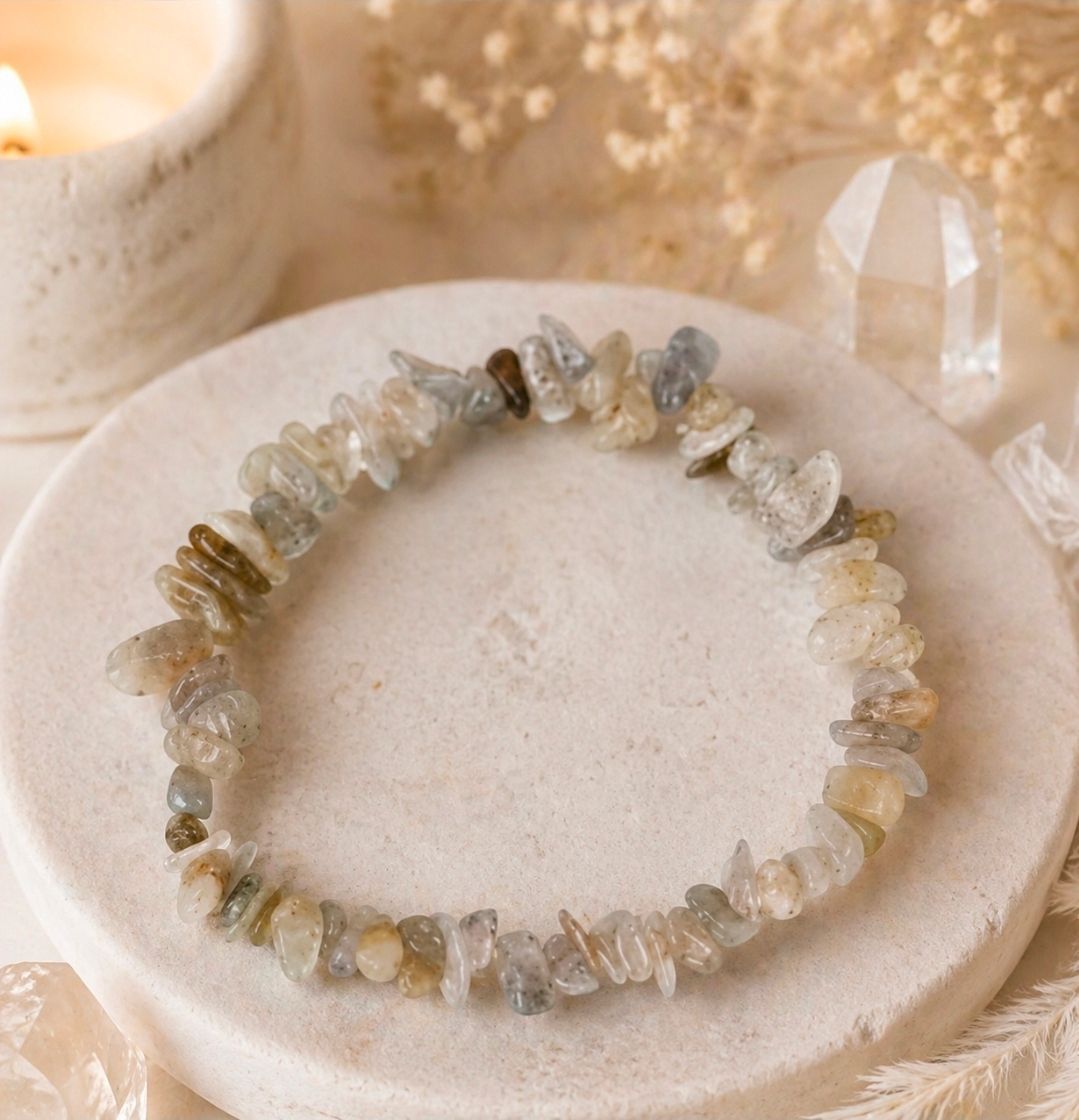 Een armband van heldere kwartskristallen op een licht rond schaaltje met een zachte beige achtergrond.