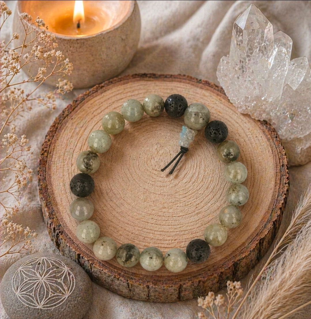 Een kralenarmband op een houten schijfje met een brandende kaars en kristallen decoratie op een zachte doek.