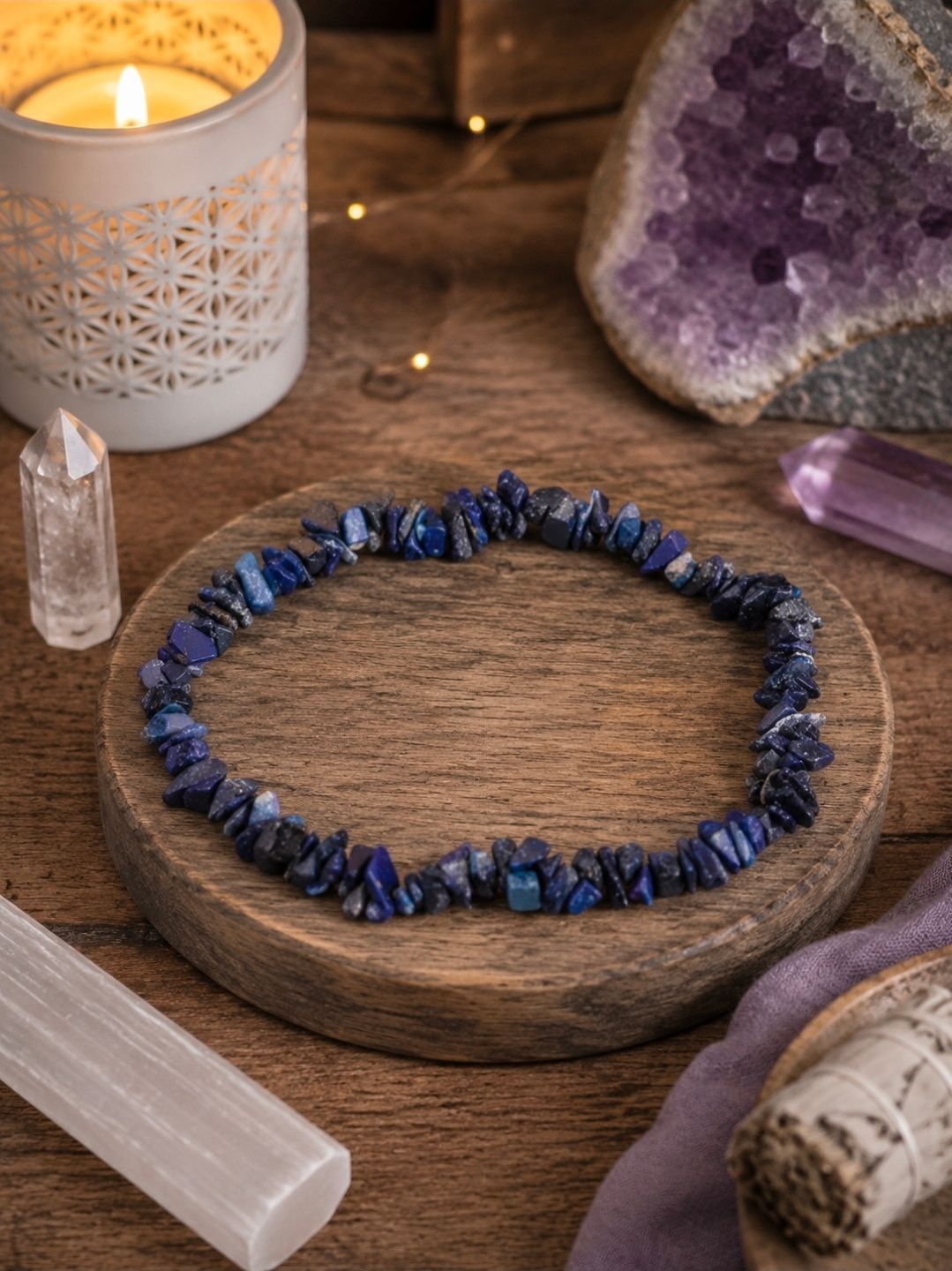 Een blauwe kralenarmband op een houten dienblad met kristallen, een brandende kaars en een amethist.