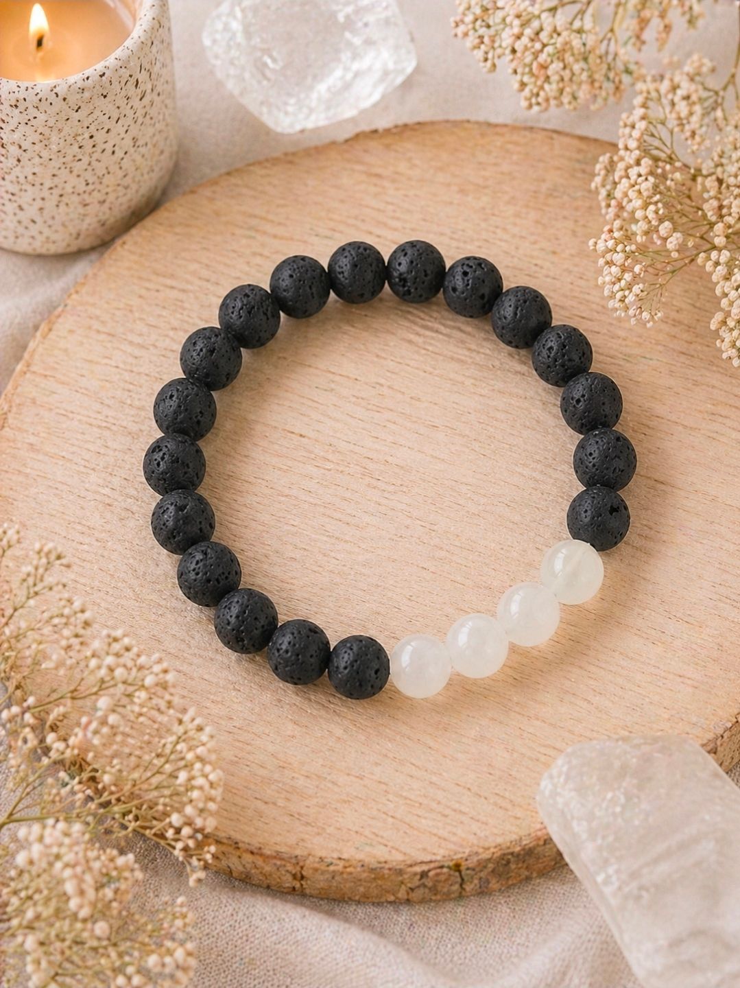 Zwarte kralenarmband met witte kralen op een houten dienblad, omringd door kristallen en gedroogde bloemen.