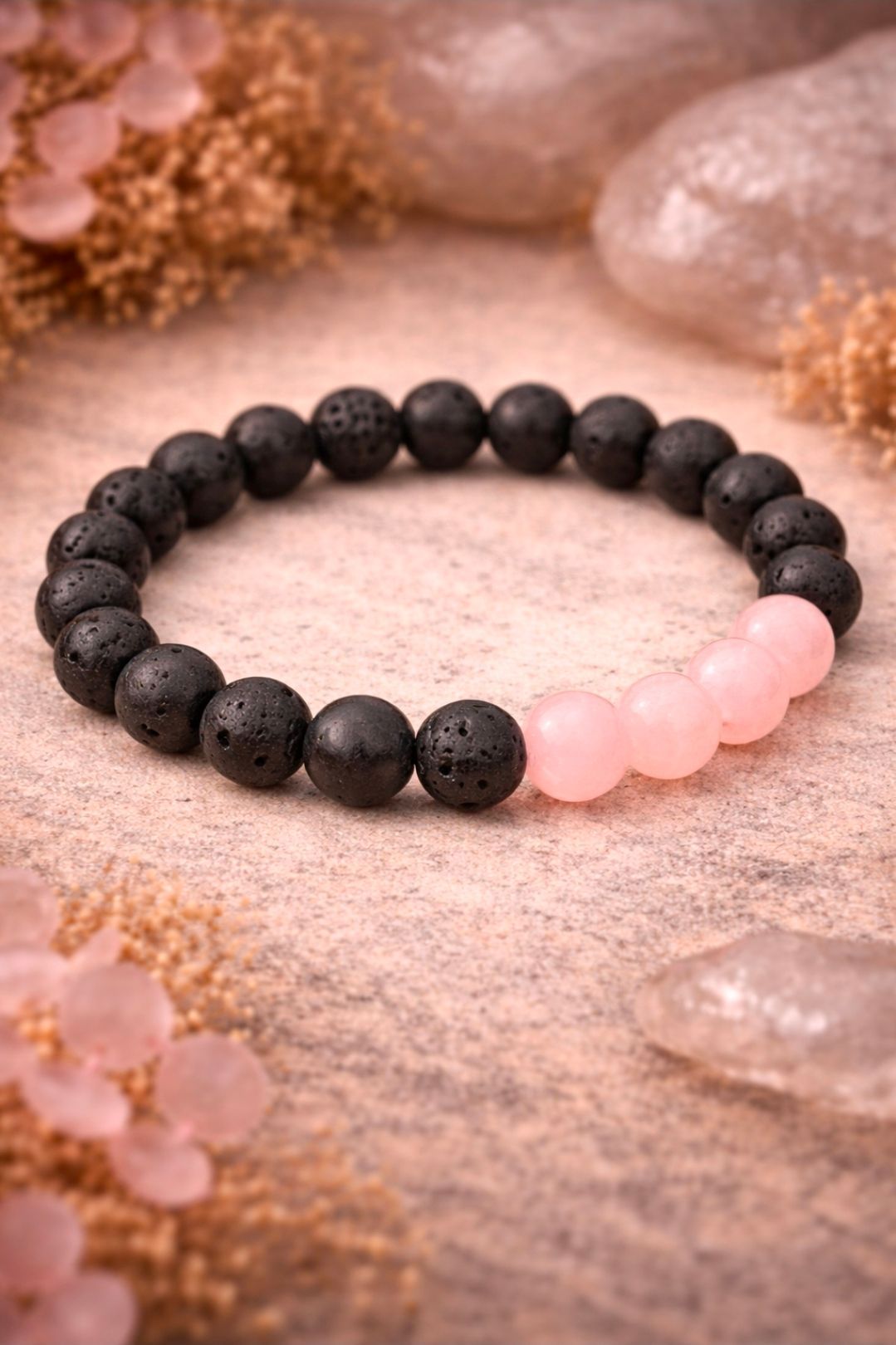 Zwarte en roze kralenarmband op een zachtroze, gestructureerde ondergrond met kristallen.