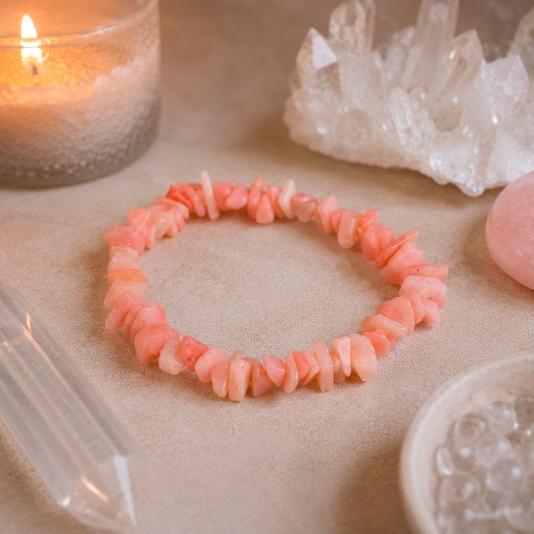 Roze kralenarmband op een zachtbeige ondergrond naast een kaars en transparante kristallen.