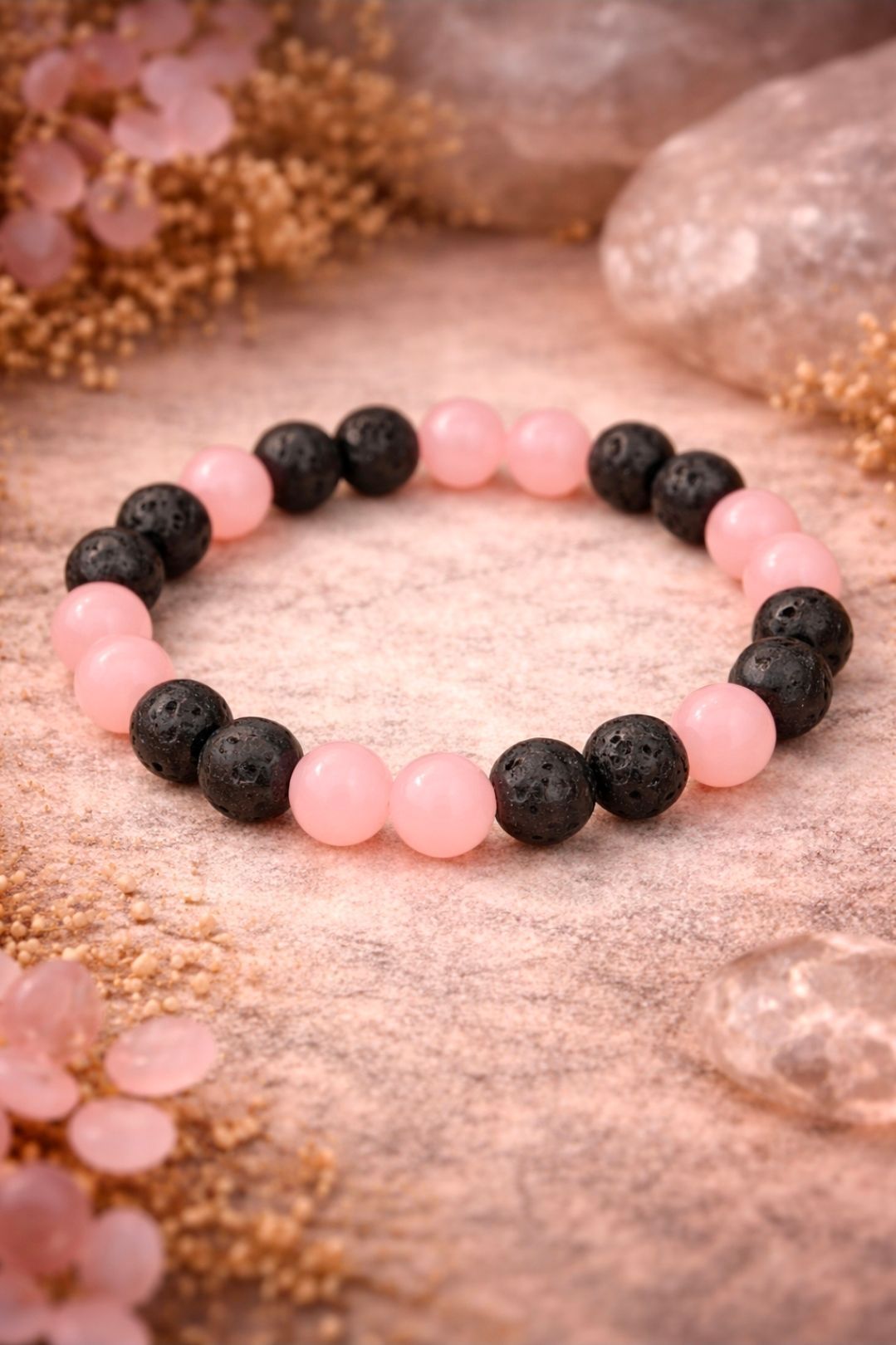 Roze en zwarte kralenarmband op een zachtroze, gestructureerde ondergrond met bloemaccenten.