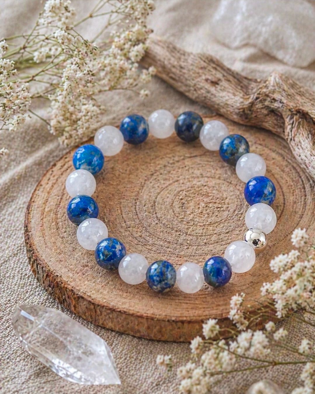 Blauw-witte kralenarmband op een ronde houten onderzetter met gedroogde bloemen en een kristal.