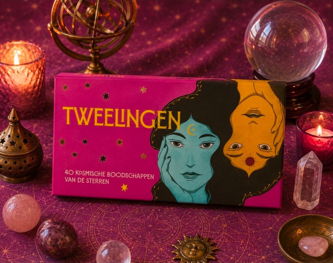 De doos van het bordspel Twelingen op een glinsterende paarse tafel met kristallen, kaarsen en decoratieve bollen.