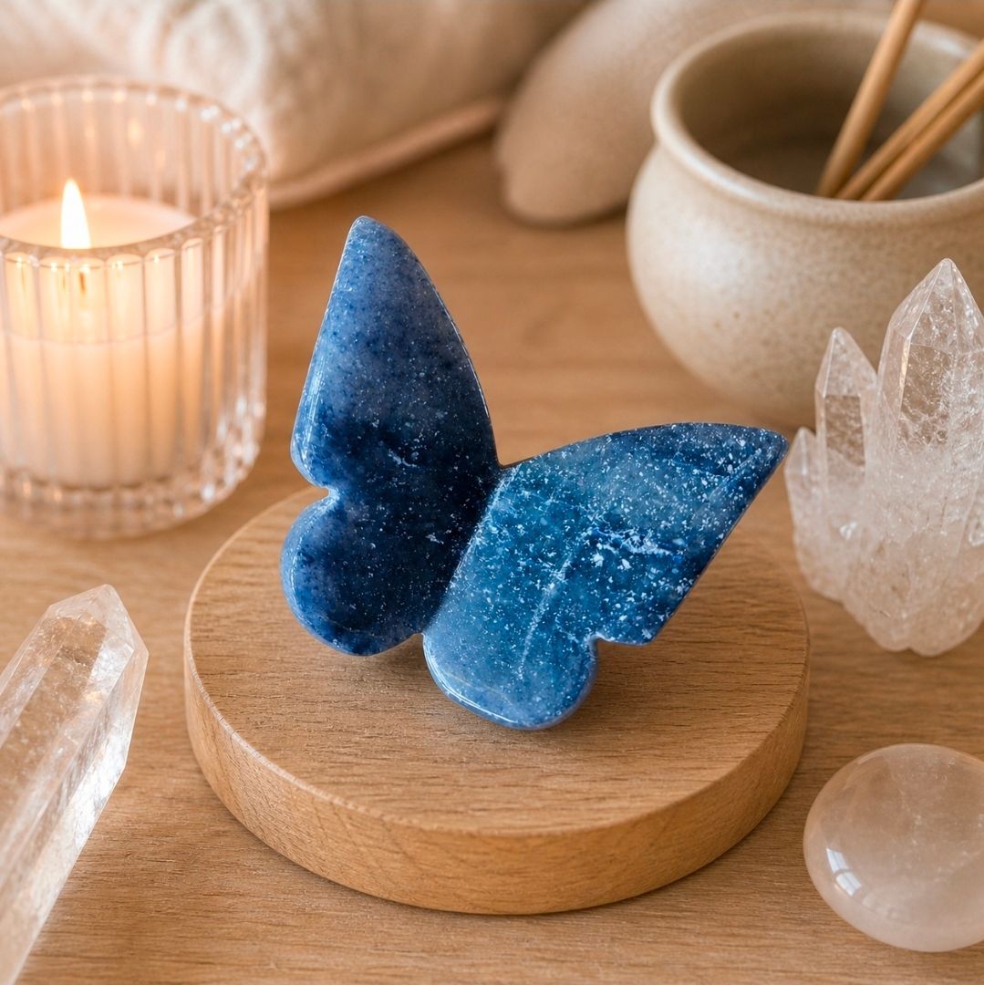 Een sculptuur van een blauwe vlinder op een houten voetstuk, omringd door kaarsen en kristallen op een tafel.