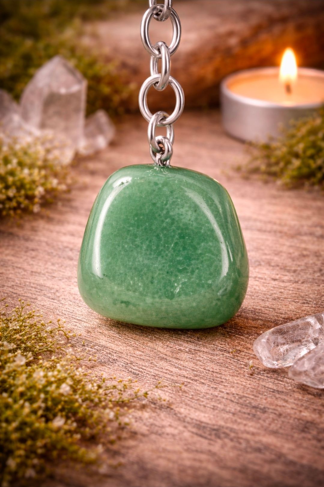 Groene stenen hanger aan een ketting, rustend op een houten ondergrond met kristallen en een brandende kaars in de buurt.