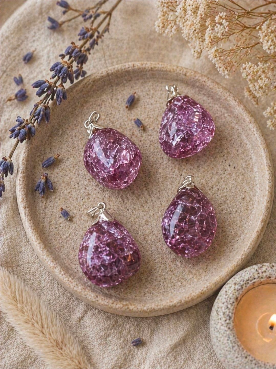 Vier paarse, kristalachtige truffels op een beige bord met gedroogde lavendel en een brandende kaars ernaast.
