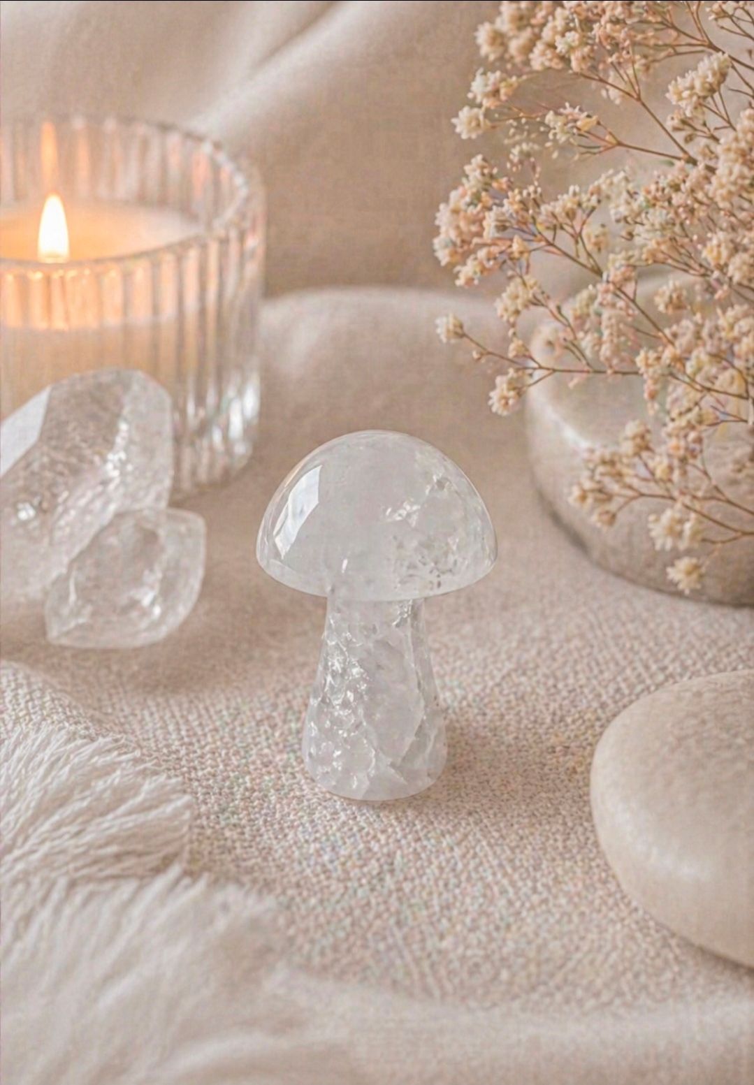 Zachtbeige stilleven met een brandende kaars, glazen paddenstoelen, gedroogde bloemen en een ronde witte steen.