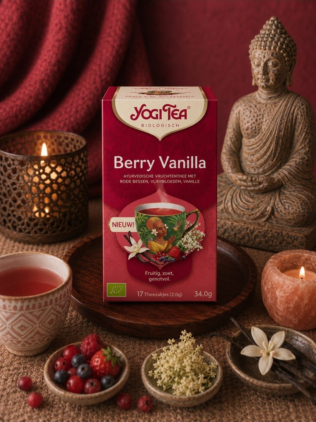 Een doos YogTea Berry Vanilla thee met bessen en theekopjes naast een Boeddhabeeld en brandende kaarsen.