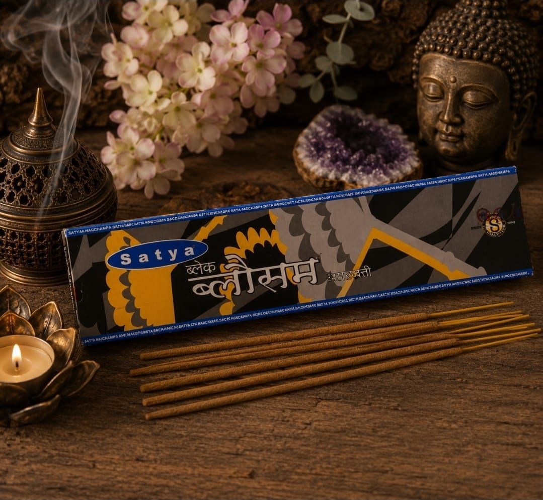 Een wierookdoos van Satya Nag Champa met brandende wierook, een kaars, een Boeddhabeeldje en bloemen op een houten tafel.