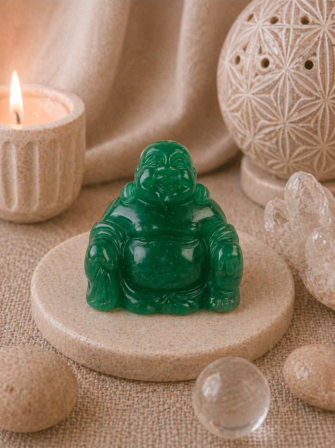 Groene jade Boeddha-figuur op een beige stenen onderzetter naast een brandende kaars en kristallen decoratie.