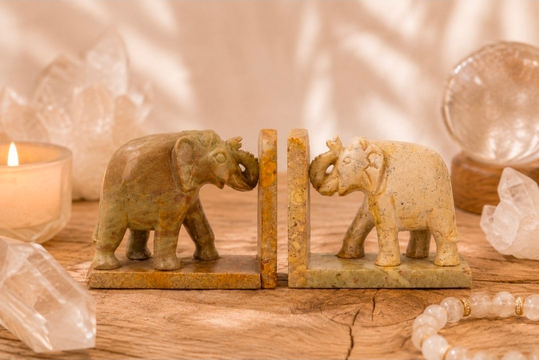 Twee olifantenbeeldjes staan ​​tegenover elkaar op een houten tafel, geflankeerd door kristallen decoraties.