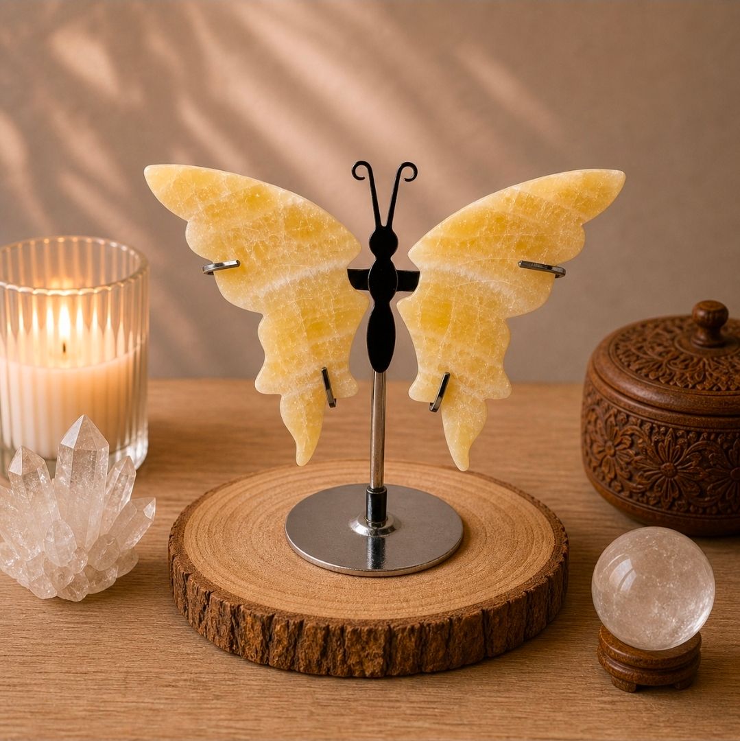 Gele, vlindervormige kaarsenhouder op een houten voet, met ernaast een brandende kaars, kristal en decoratieve voorwerpen.
