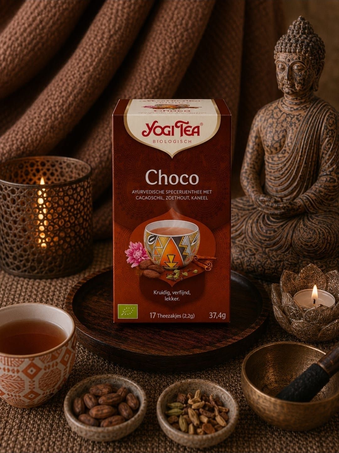 Yogi Tea Choco-doos met een Boeddhabeeldje, kaarsen en thee-ingrediënten op een warme bruine achtergrond.