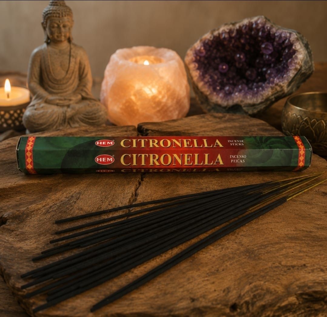 Boeddhabeeld met brandende kaarsen, kristallen, citronella-wierookstokjes en een brandend wierookkegeltje op een houten tafel.