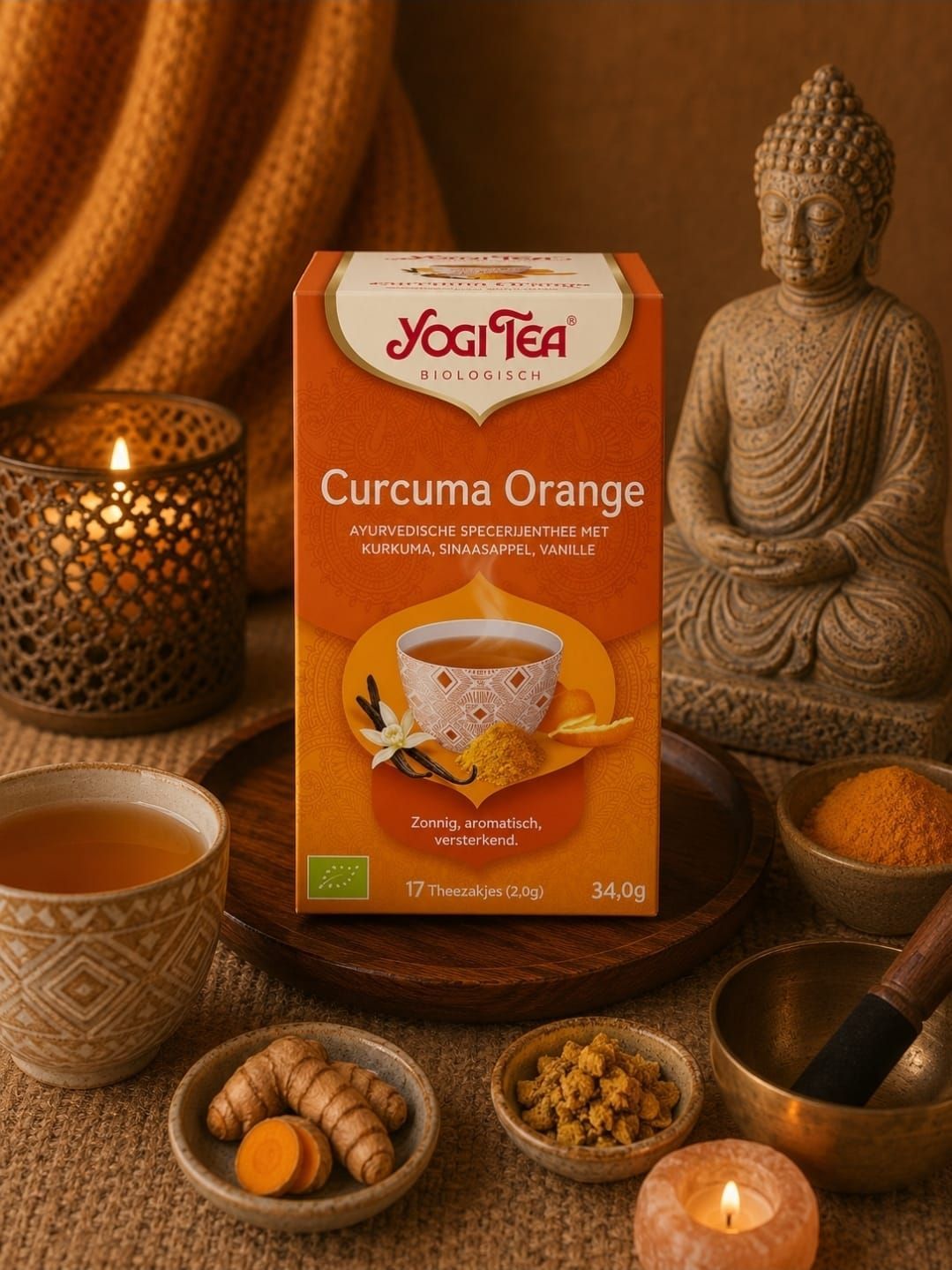 Een doosje Yogi Tea Curcuma Orange te midden van kaarsen, een theekopje, specerijen en een Boeddhabeeld