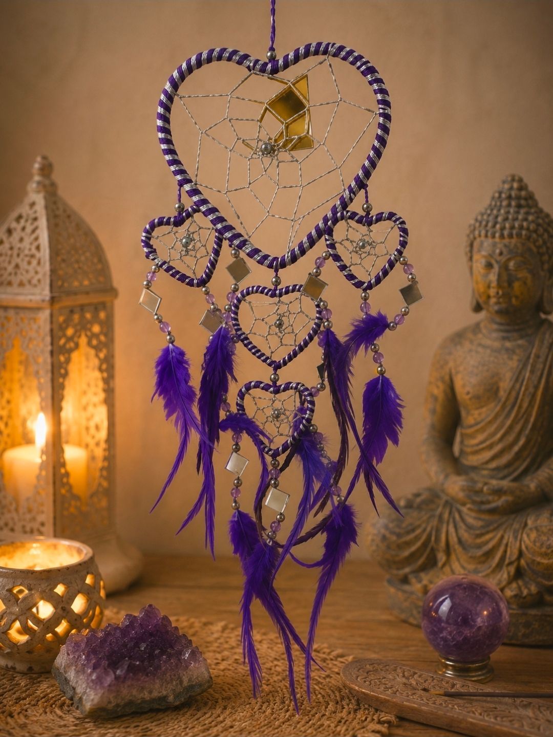Paarse, hartvormige dromenvanger met veren, kristallen en Boeddhabeelden in een warm verlichte, spirituele omgeving.