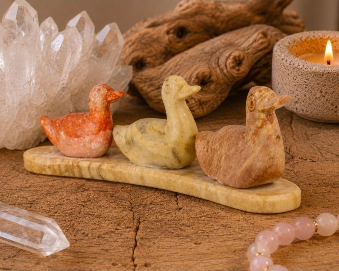 Drie kleine keramische vogeltjes op een houten dienblad naast kristallen en een brandende kaars.