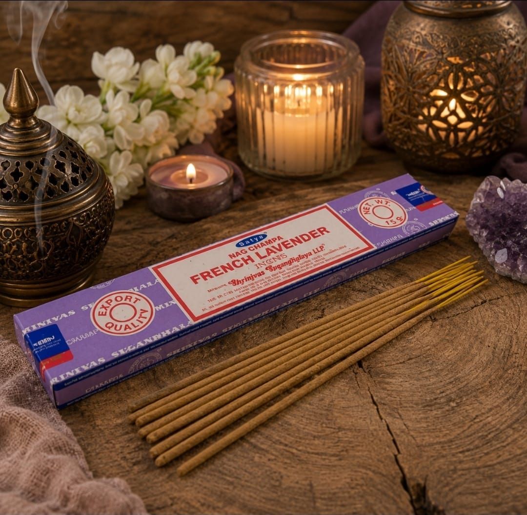Wierookstokjes en een doos op een houten tafel met brandende kaarsen en witte bloemen in een warme, decoratieve setting.