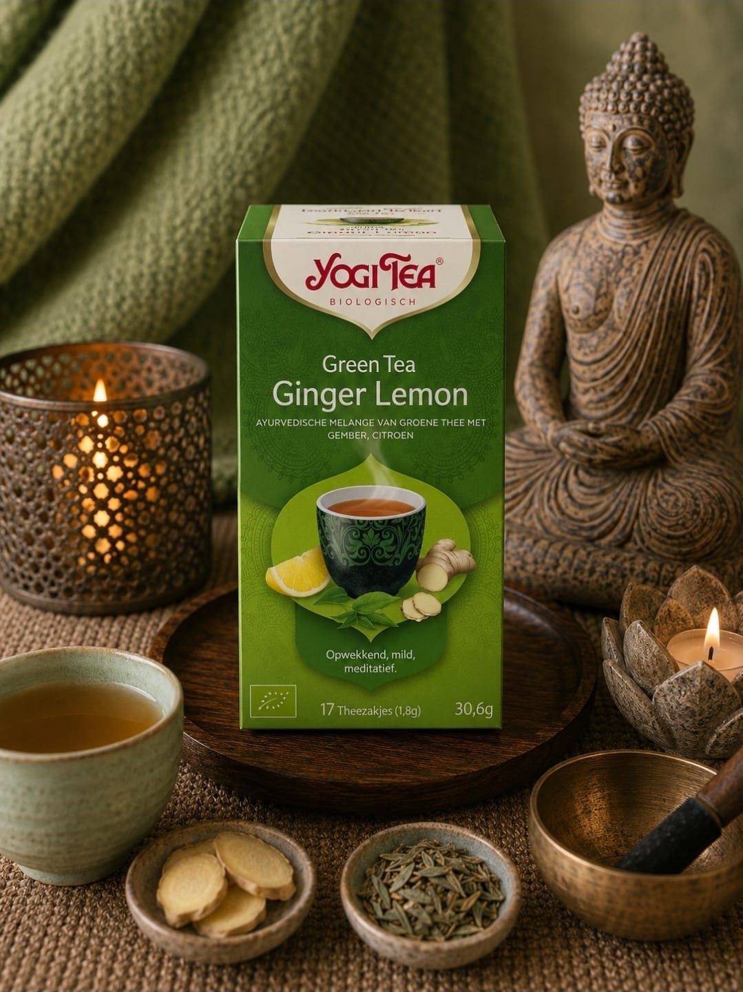 Een doos Yogi Tea Ginger Lemon met theeservies, plakjes gember en een Boeddhabeeldje op een warme, door kaarsen verlichte tafel.