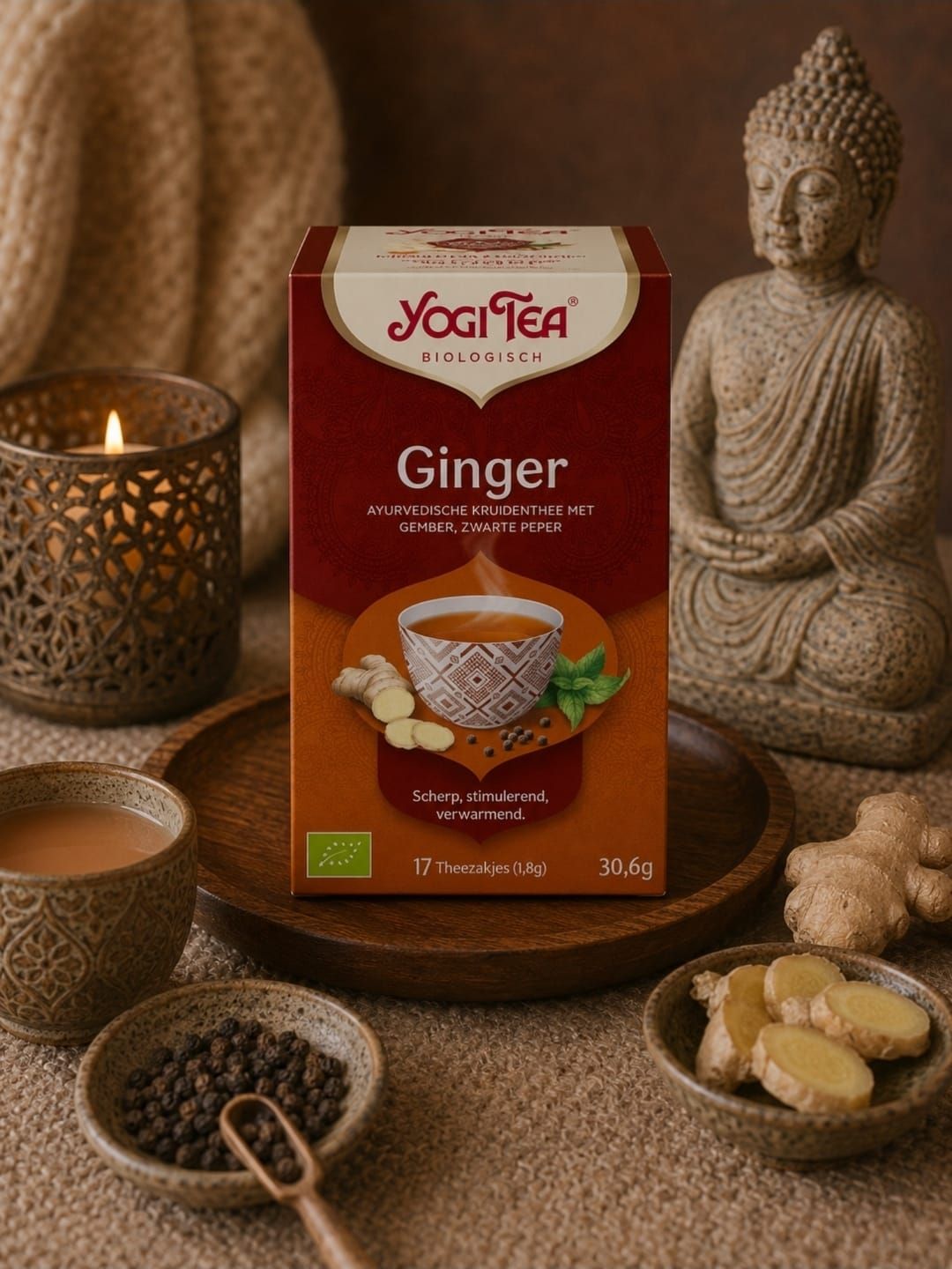 Een doosje Yogi Tea Ginger op een rustiek dienblad naast een brandende kaars, een Boeddhabeeldje en stukjes gember.