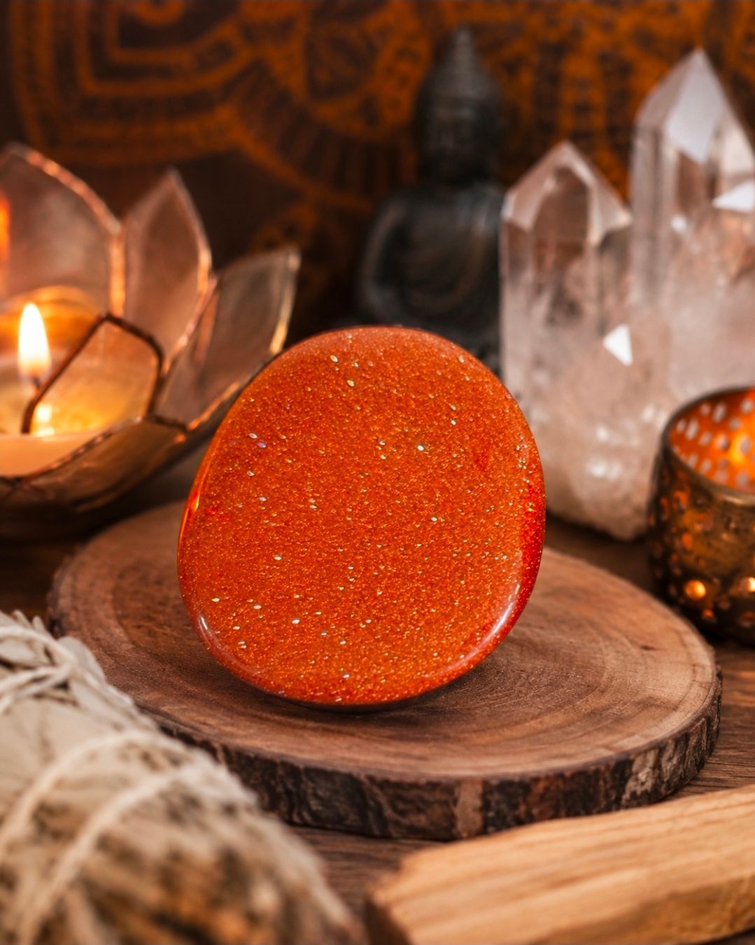 Oranje glinsterende steen op een houten plaat, omringd door kaarsen en heldere kristallen in een warme, decoratieve setting.