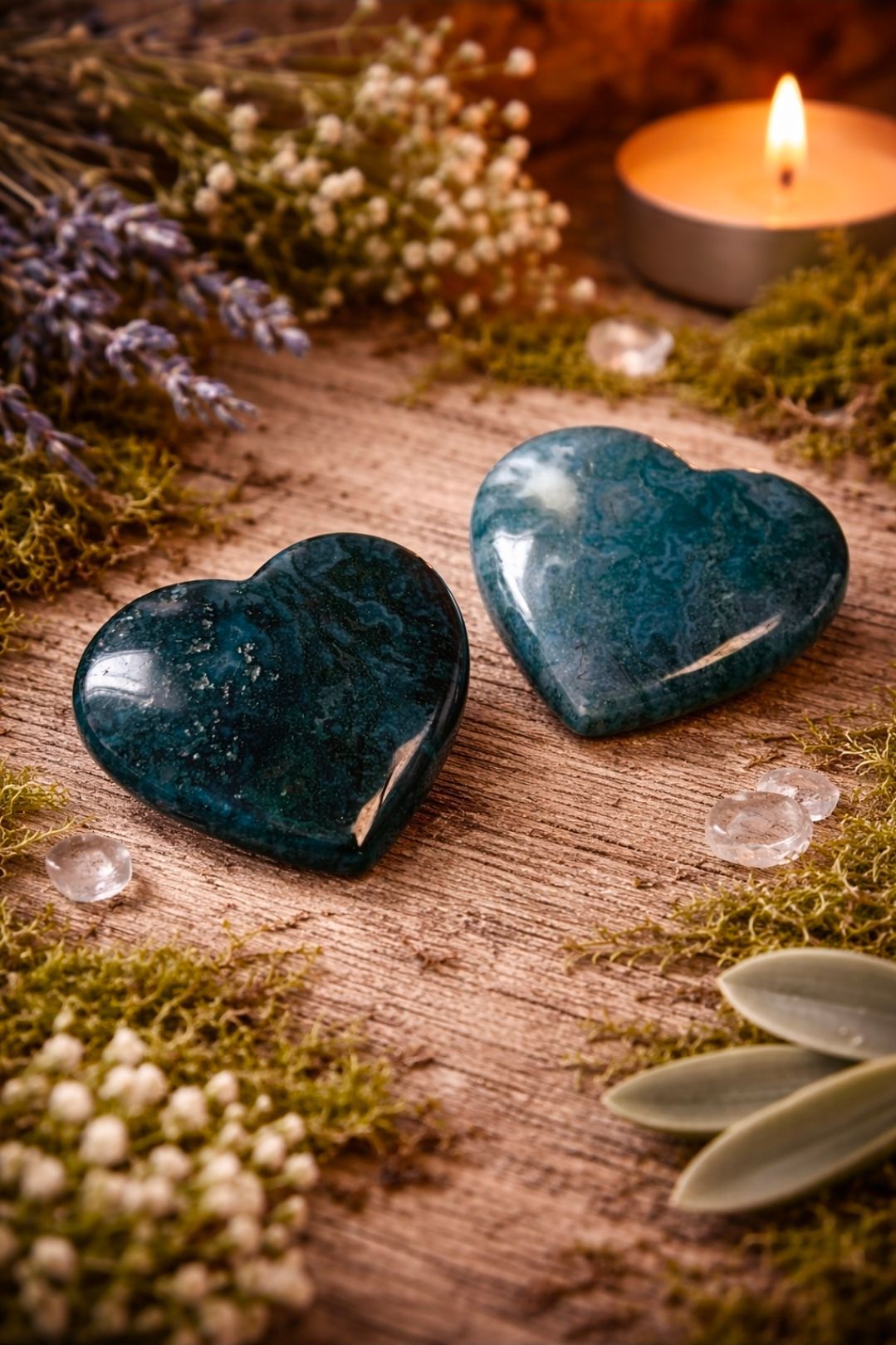 Twee turquoise hartvormige stenen op met mos begroeid hout, naast een brandende kaars en kleine bloemen.