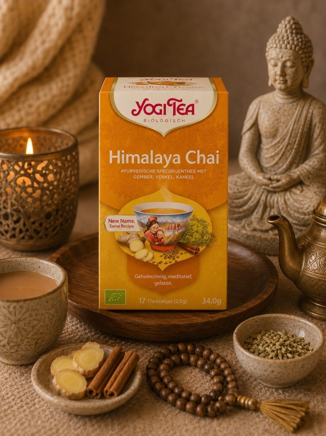 Een doos Yogi Tea Himalaya Chai naast een brandende kaars, een Boeddhabeeld en thee-ingrediënten op een warme tafel.