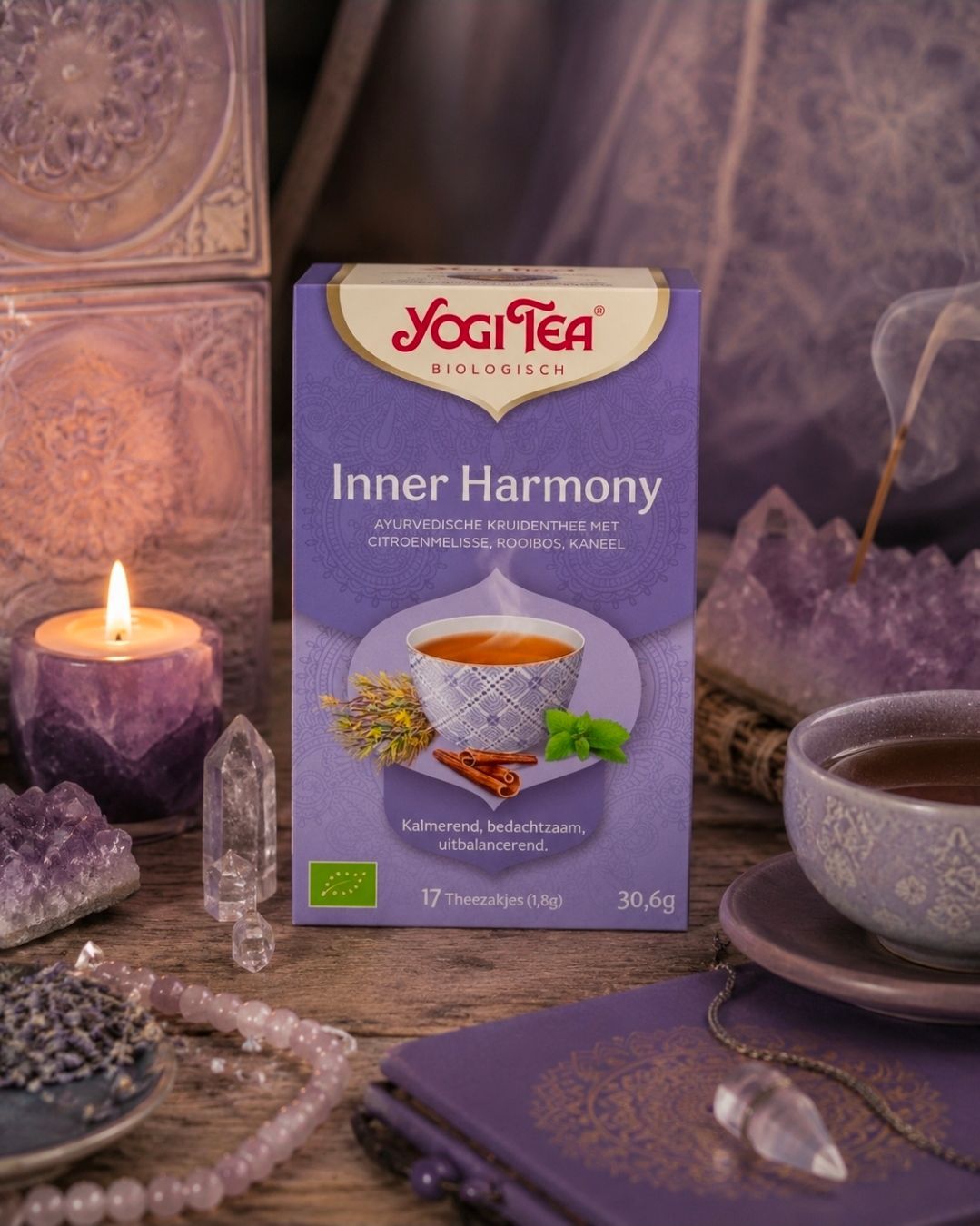 Een doosje Yogi Tea Inner Harmony op een paarse tafel in spa-stijl met een kaars, kristallen en een theekopje.