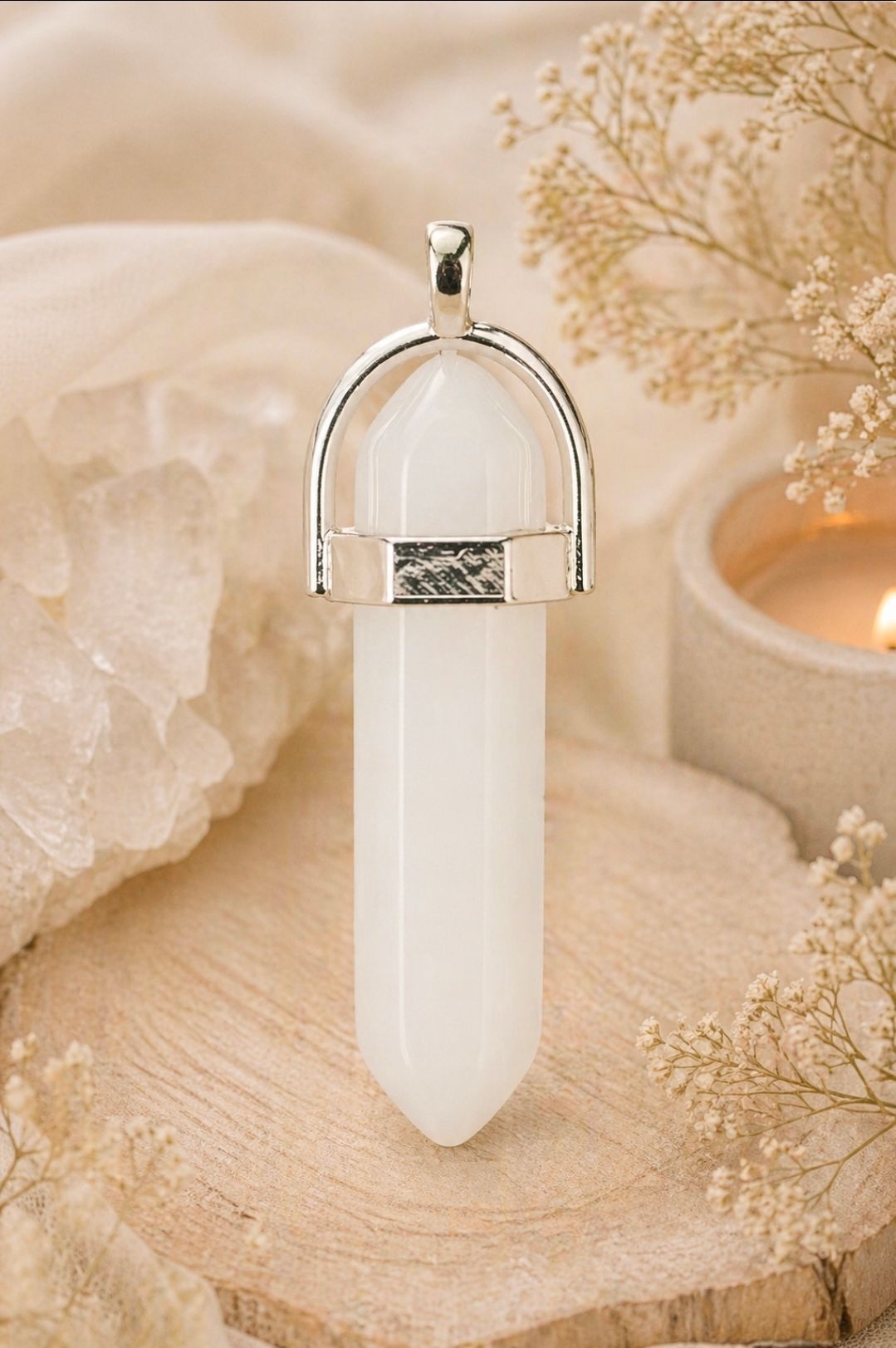 Witte kristallen hanger met zilveren dop op zachtbeige stof en gedroogde bloemen, in een warme, neutrale omgeving.