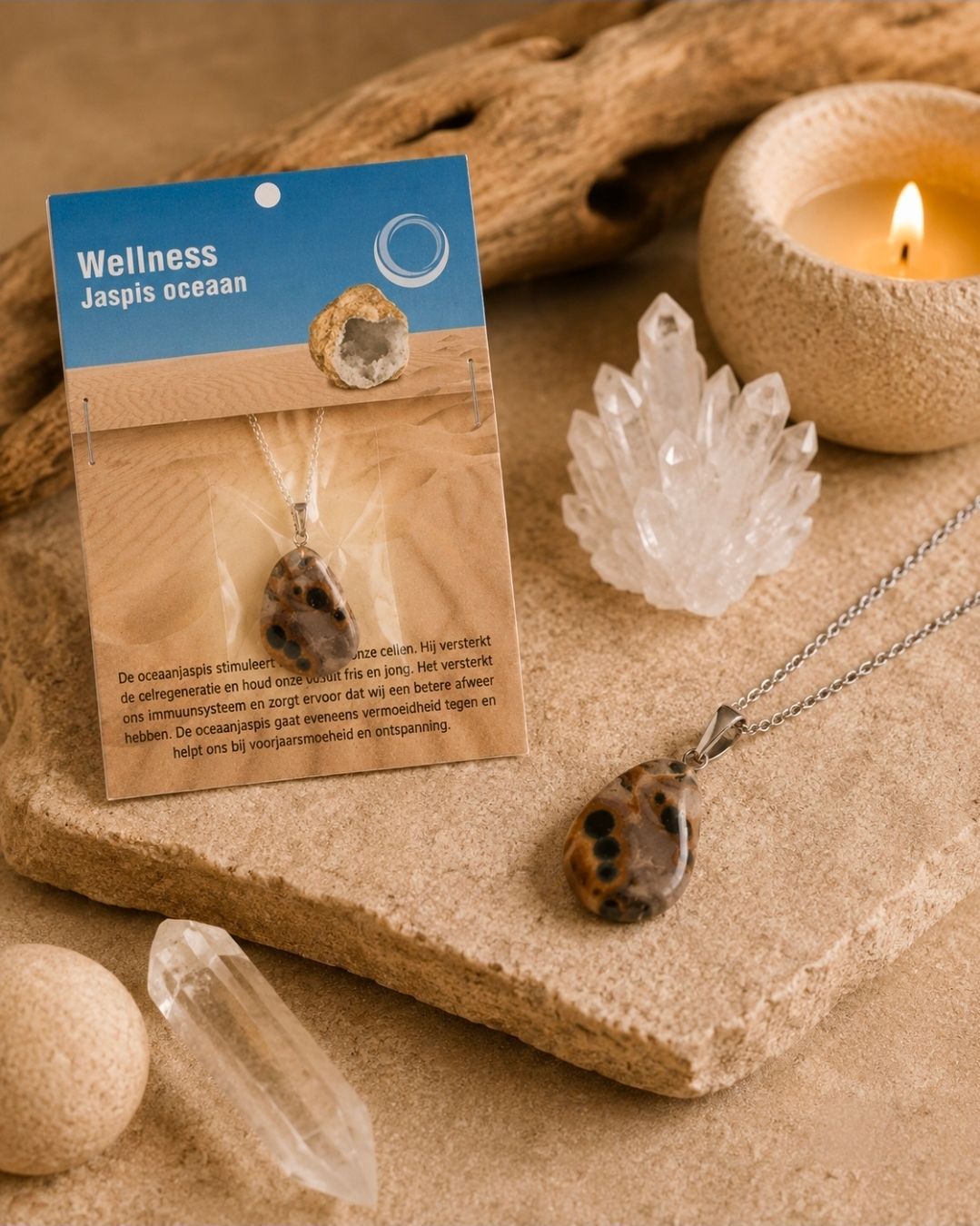 Wellness jaspis ketting tentoongesteld op zand met kristallen, kaars en een achtergrond van lichtbruine steen.