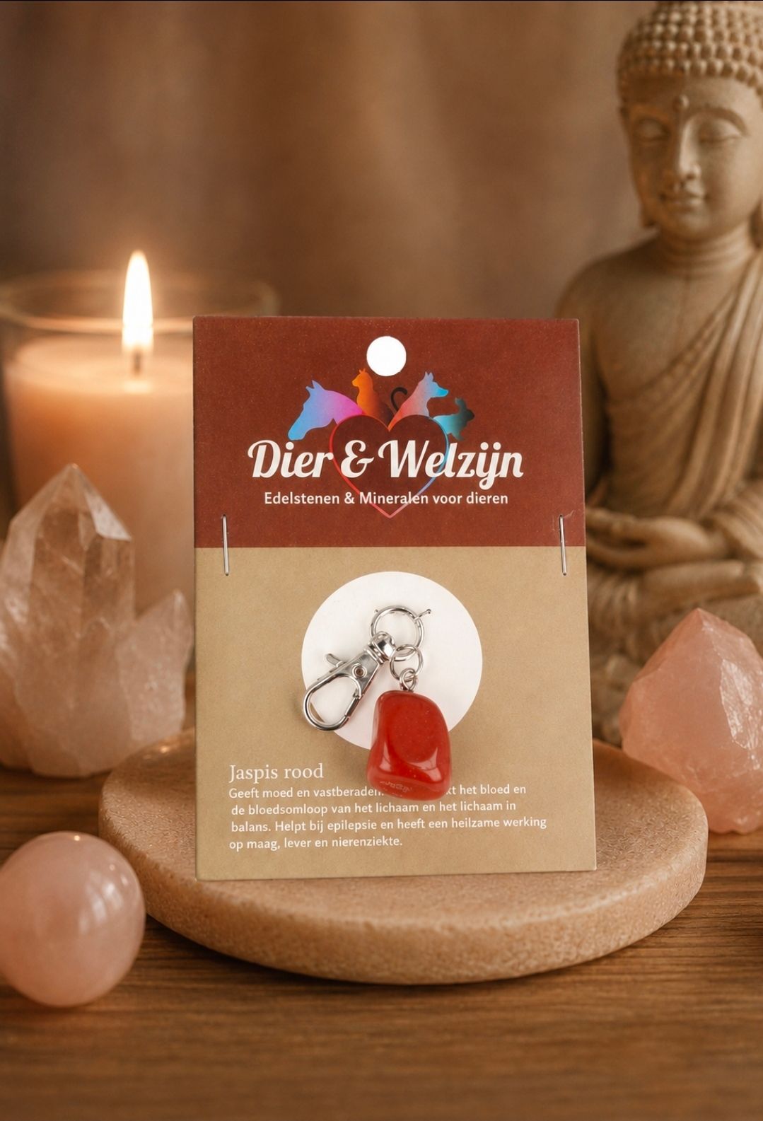 Rood-crème sieradenkaartje op een houten standaard met een Boeddhabeeld, kristallen en een kaars op de achtergrond.