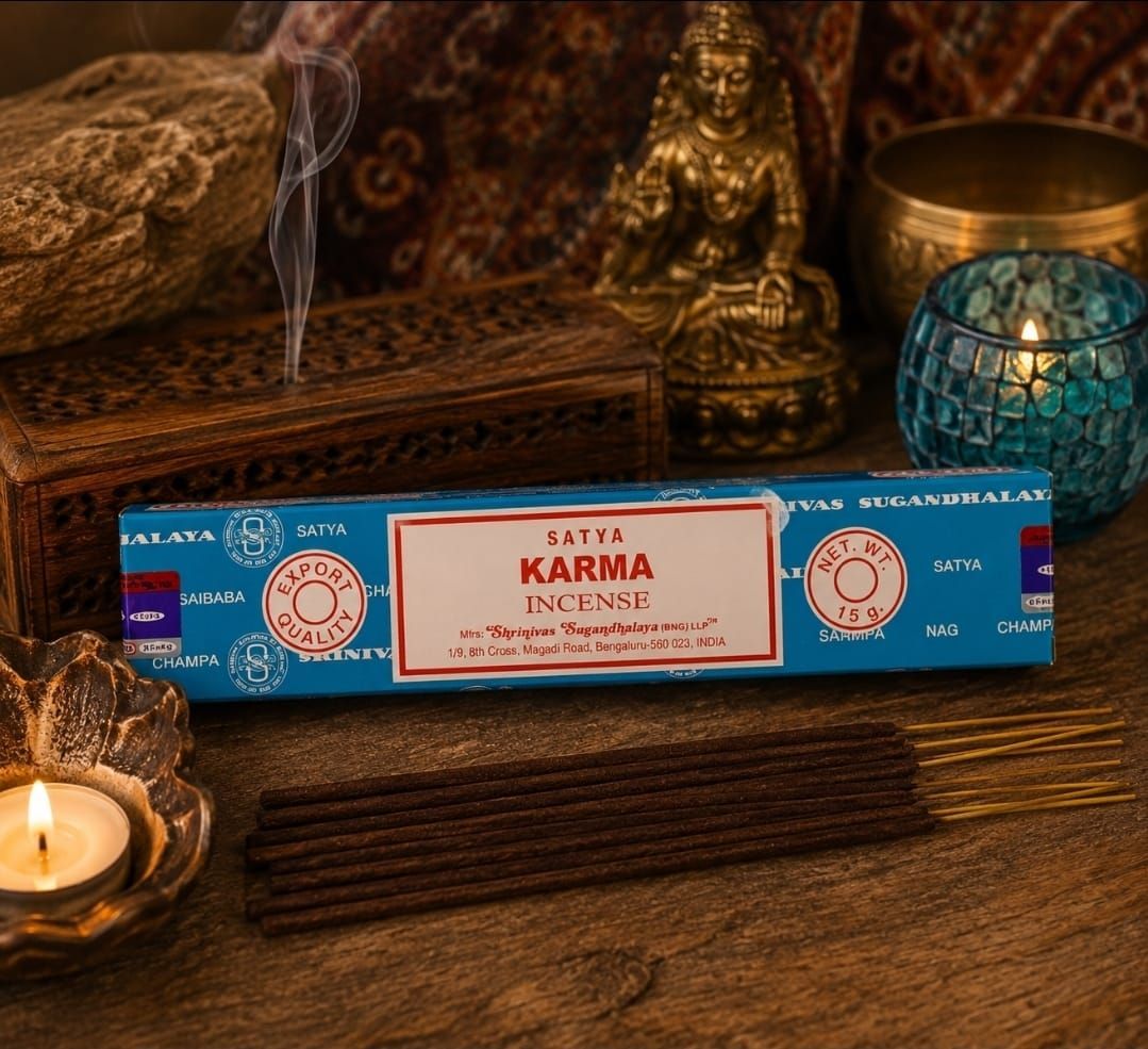Een doosje blauwe KARMA-wierook op een houten tafel met een brandende kaars, rook en decoratieve beeldjes.