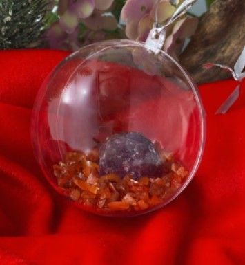 Doorzichtig glazen terrarium met oranje steentjes en een paars kristal erin.