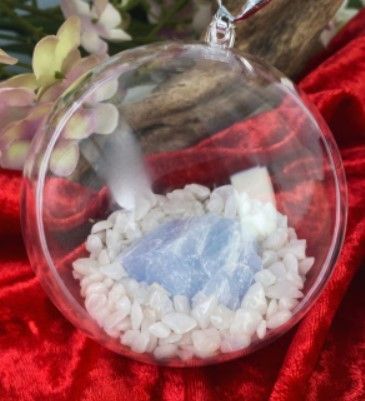 Hangend, transparant bolvormig terrarium met witte kiezels en een blauwe, kristalachtige steen erin.