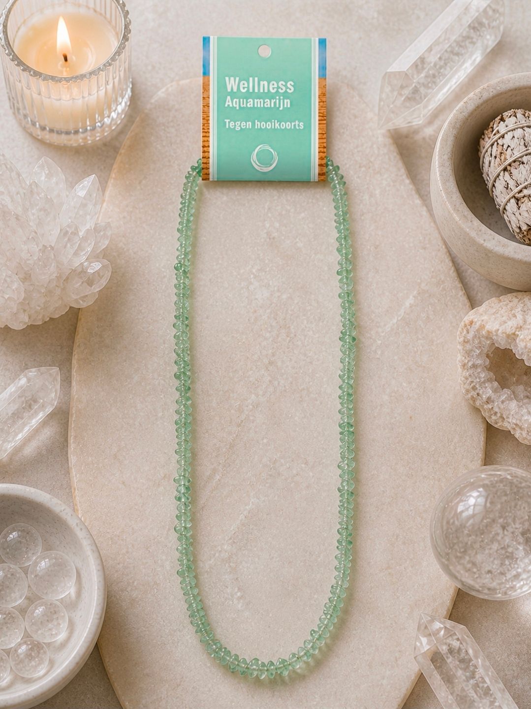 Mintgroene kralenketting op een beige, gestructureerde ondergrond met kaarsen en kristallen decoratie eromheen.