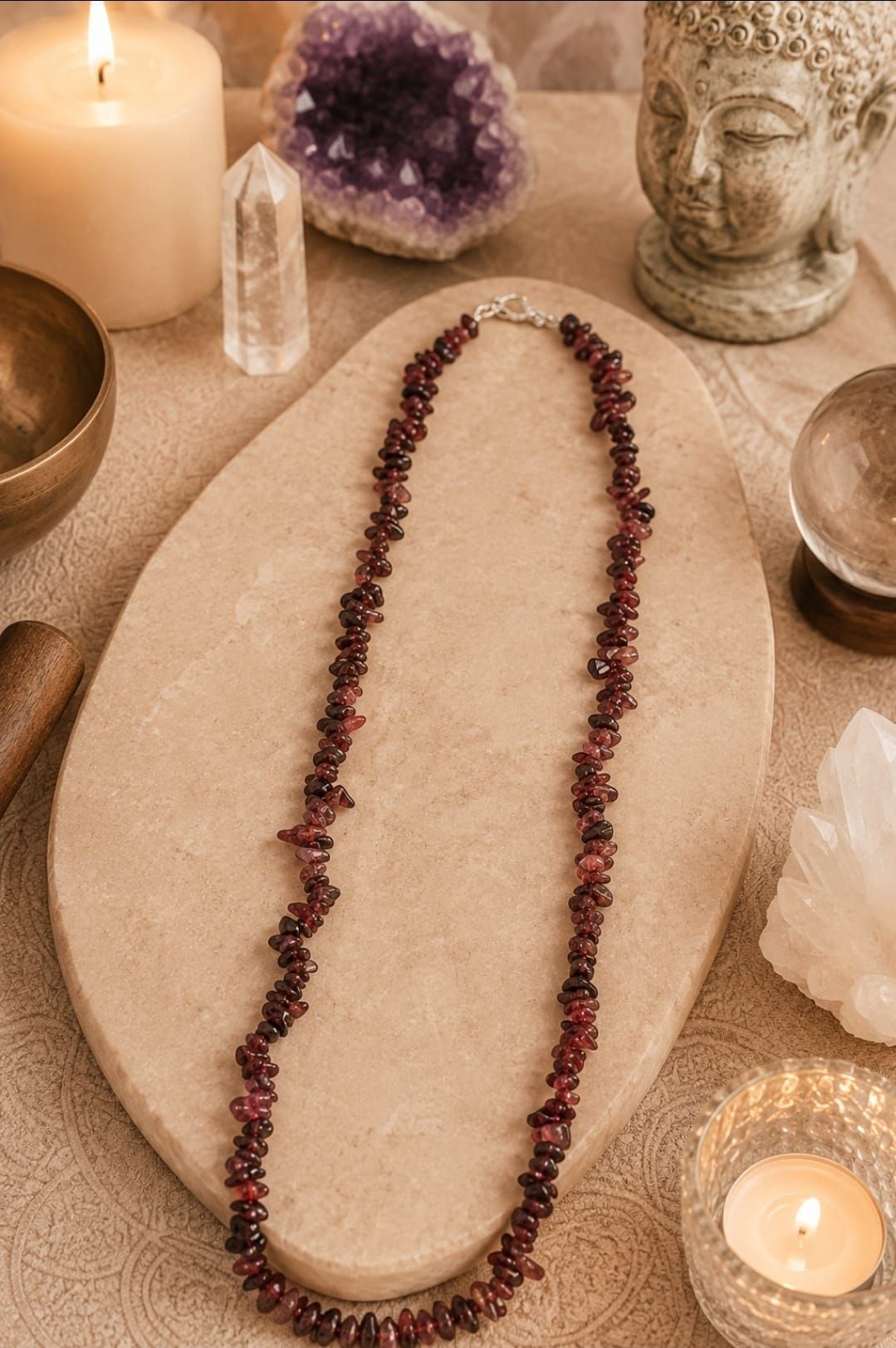 Een kralenketting op een stenen dienblad met kaarsen, kristallen en een Boeddhabeeld in een spa-achtige omgeving.