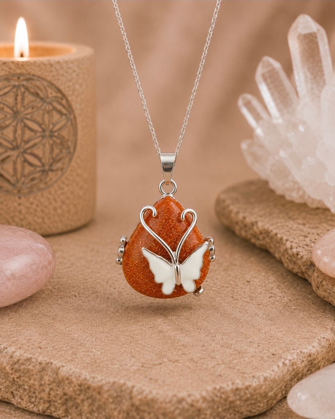 Amberkleurige vlinderhanger aan een zilveren ketting, tentoongesteld op een zandkleurige steen