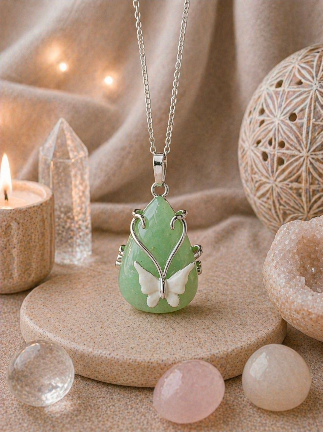 Groene druppelvormige hanger met een witte vlinder op een beige ondergrond, omringd door kaarsen en kristallen.