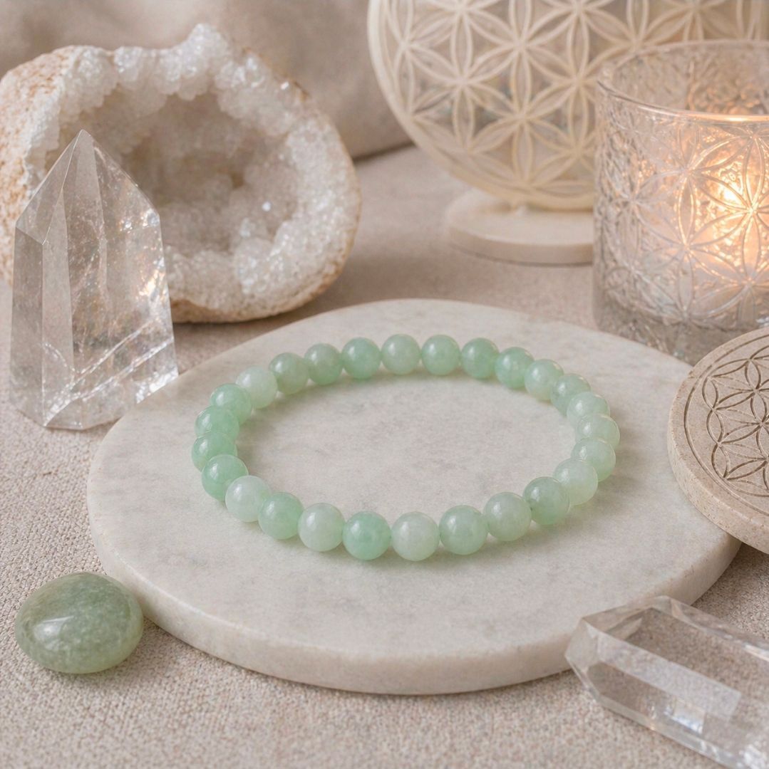 Een mintgroene kralenarmband op een wit stenen dienblad met kristallen en een brandende kaars.