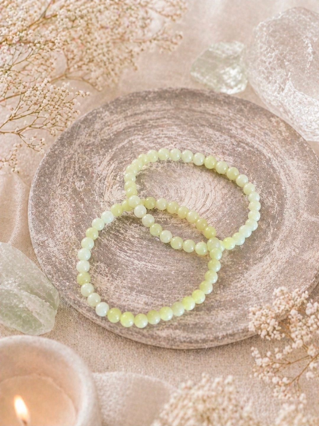Twee lichtgroene kralenarmbandjes op een zachtroze decoratief dienblad met kaarsen en gedroogde bloemen.